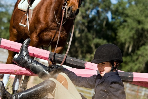 Young female equestrian falls off horse while trying to clear an obstacle in competition